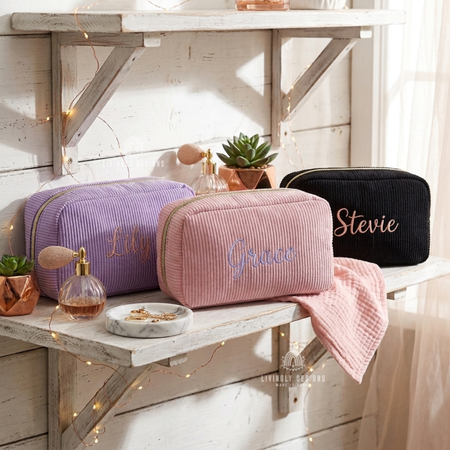 Purple, pink, and black corduroy makeup bags named Lily, Grace, and Stevie on a shelf.