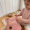 Child playing near a pink teddy bear backpack named Emily.
