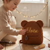 Child touching a brown teddy bear backpack named Eloise.
