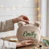 Hands placing lipstick into a cream teddy bear pouch named Emily.