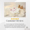 5-star customer review graphic featuring a white textured knit baby romper laid flat on a white faux fur rug, accented with pink flower shoulder details and the name Sarah embroidered in pink.