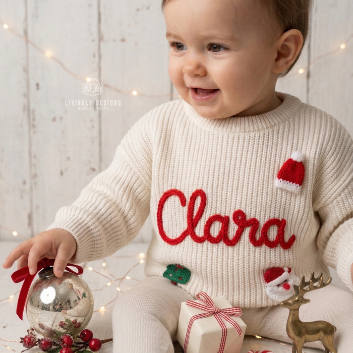Smiling child wearing a cream knitted Christmas sweater personalized with the name “Clara” and festive Santa, Christmas tree, and holiday designs.
