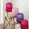 Four backpacks in pink, light pink, purple, and hot pink with sparkly tulle ballerina dress appliqués, personalized with the names "Valerie," "Mia," "Kylie," and "Jenna," displayed on a wooden ladder