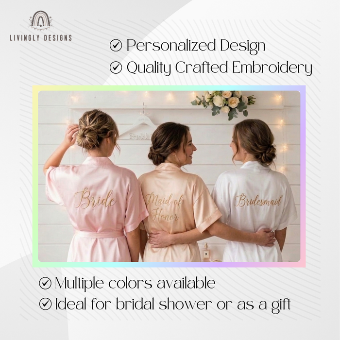 Three women wearing personalized satin bridal robes labeled Bride, Maid of Honor, and Bridesmaid.