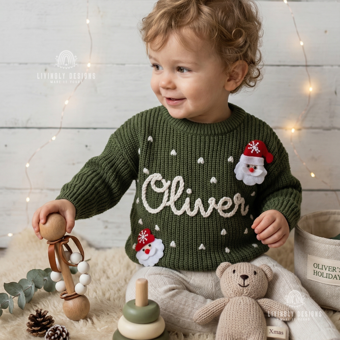 Smiling child wearing a green knitted Christmas sweater personalized with the name “Oliver” and festive Santa and snowflake designs.