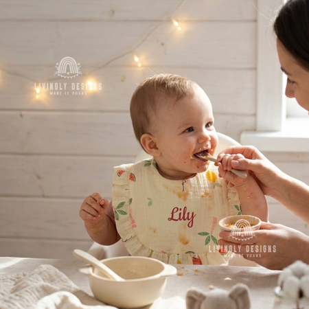 Baby wearing floral print bib named Lily being fed