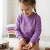 Smiling girl wearing a purple sweatshirt personalized with the name "Chloe" in colorful floral lettering