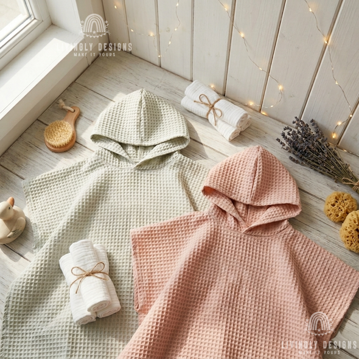 Sage green and dusty pink kids hooded waffle poncho bathrobes laid flat on a white wooden surface alongside rolled towels, a brush, and bath accessories.