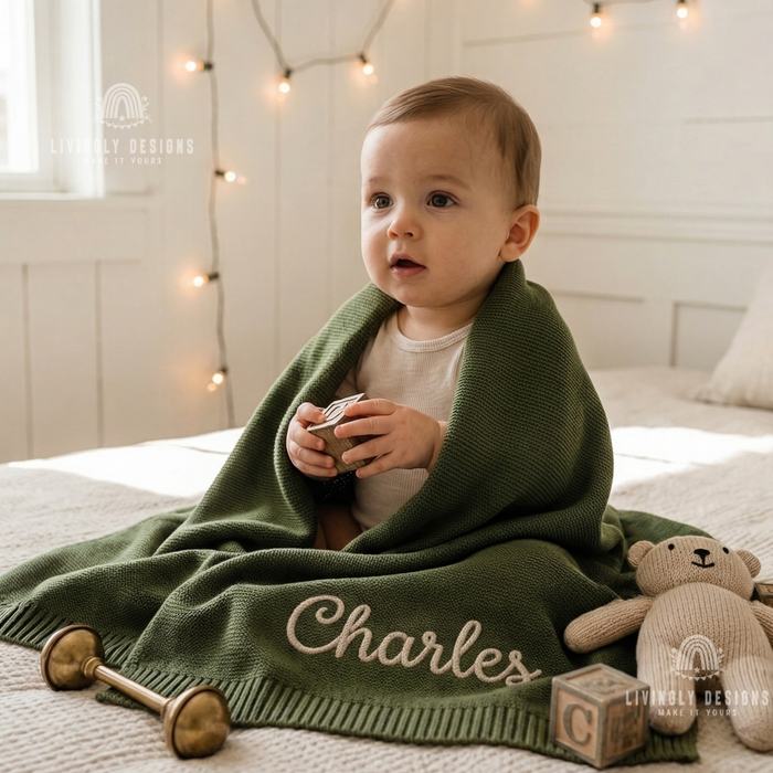 Baby wrapped in a green personalized blanket named Charles, sitting next to a plush teddy bear and wooden blocks.