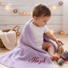 Baby wrapped in a lavender personalized blanket named Hazel, sitting next to a stuffed deer toy.