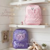 Pink and purple backpacks with sparkly tulle ballerina dress appliqués, personalized with the names "Zara" and "Riley," displayed on a shelf