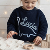 Navy sweater named Lucia on a girl playing at a table.