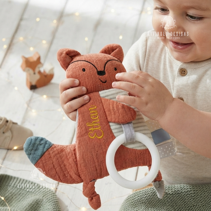 Baby holding a rust-colored fox-shaped comforter with a teething ring, personalized with the name "Ethan"