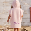 Back view of a toddler wearing a light pink hooded waffle poncho bathrobe custom embroidered with the name Eloise.