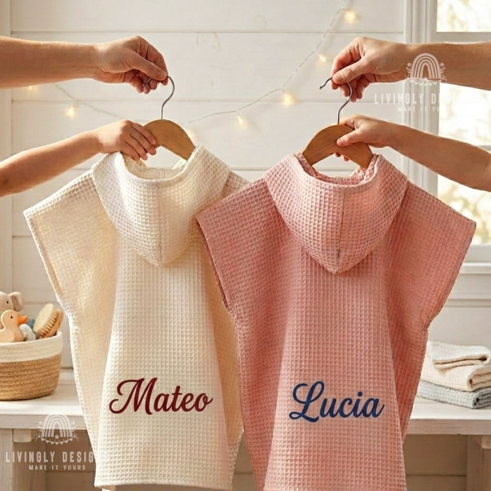 Two personalized kids waffle hooded bathrobes in cream embroidered with Mateo and pink embroidered with Lucia held on wooden hangers.