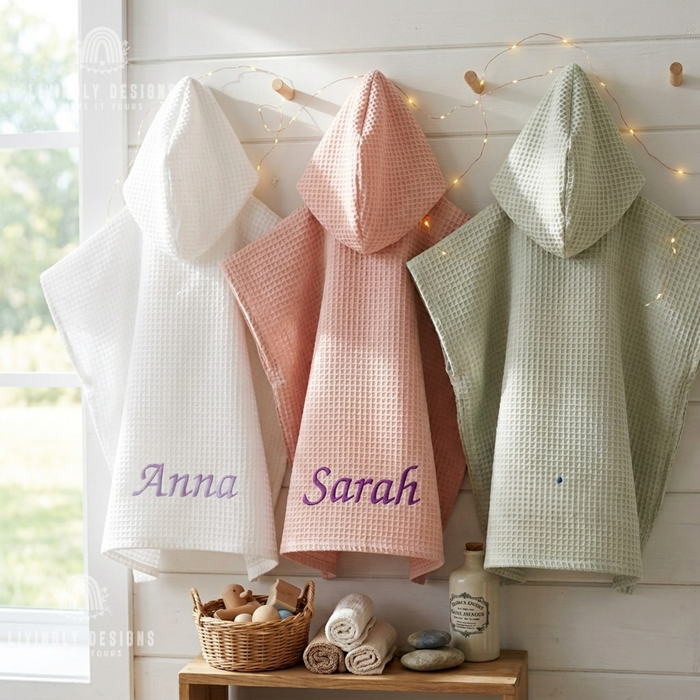 Three custom embroidered kids hooded waffle bathrobes hanging on wooden pegs in white embroidered with Anna, pink embroidered with Sarah, and sage green.