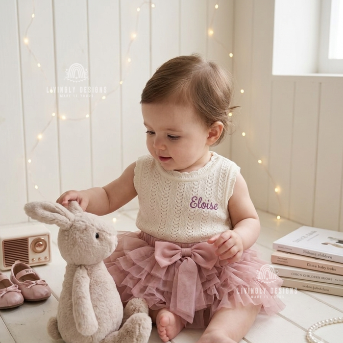 Baby wearing a cream knit romper personalized with the name "Eloise"