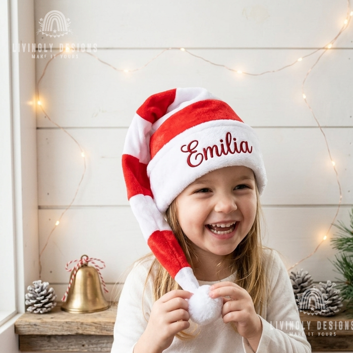 Girl wearing a red and white striped long Santa hat with the name "Emilia"