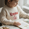 Young girl wearing a cream knitted sweater personalized with the name "Emma"