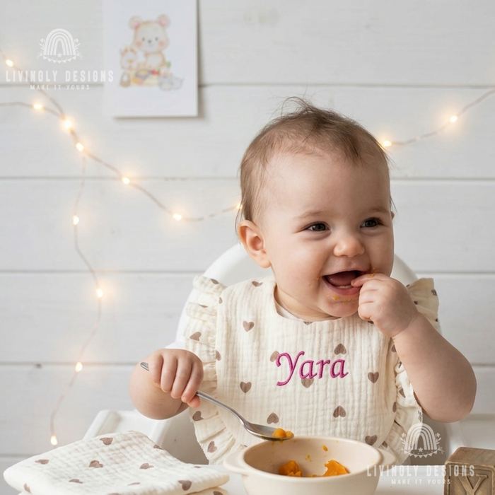 Baby wearing heart print bib named Yara 

