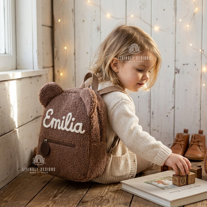 Child wearing a brown teddy bear backpack named Emilia.