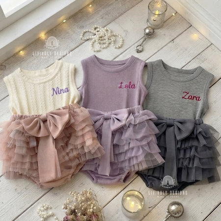 Cream, purple, and gray tank-top rompers with ruffled tutu bottoms and bows, personalized with the names "Nina," "Lola," and "Zara"
